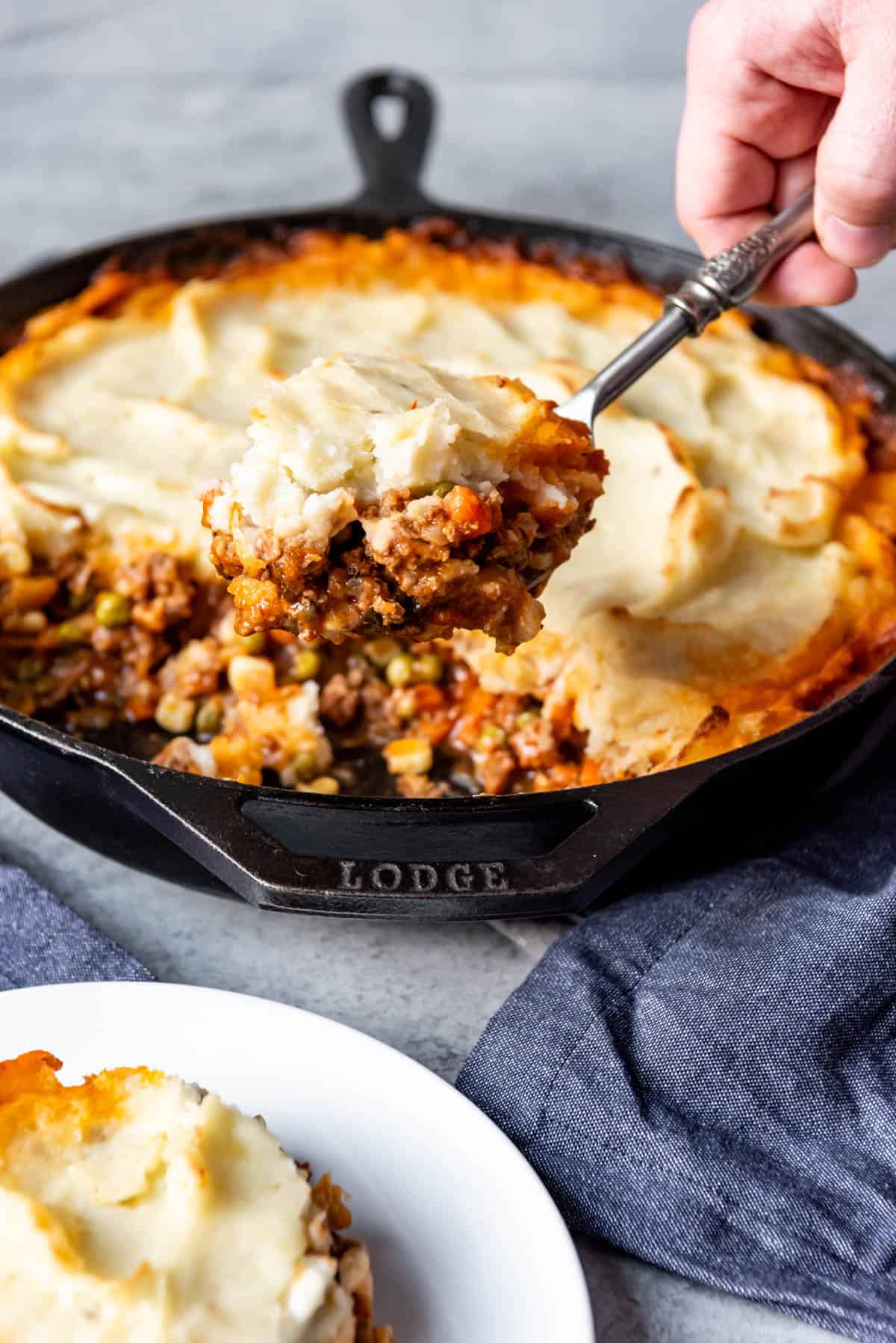 A hand holding a spoonful of shepherds pie above the cast iron skillet.