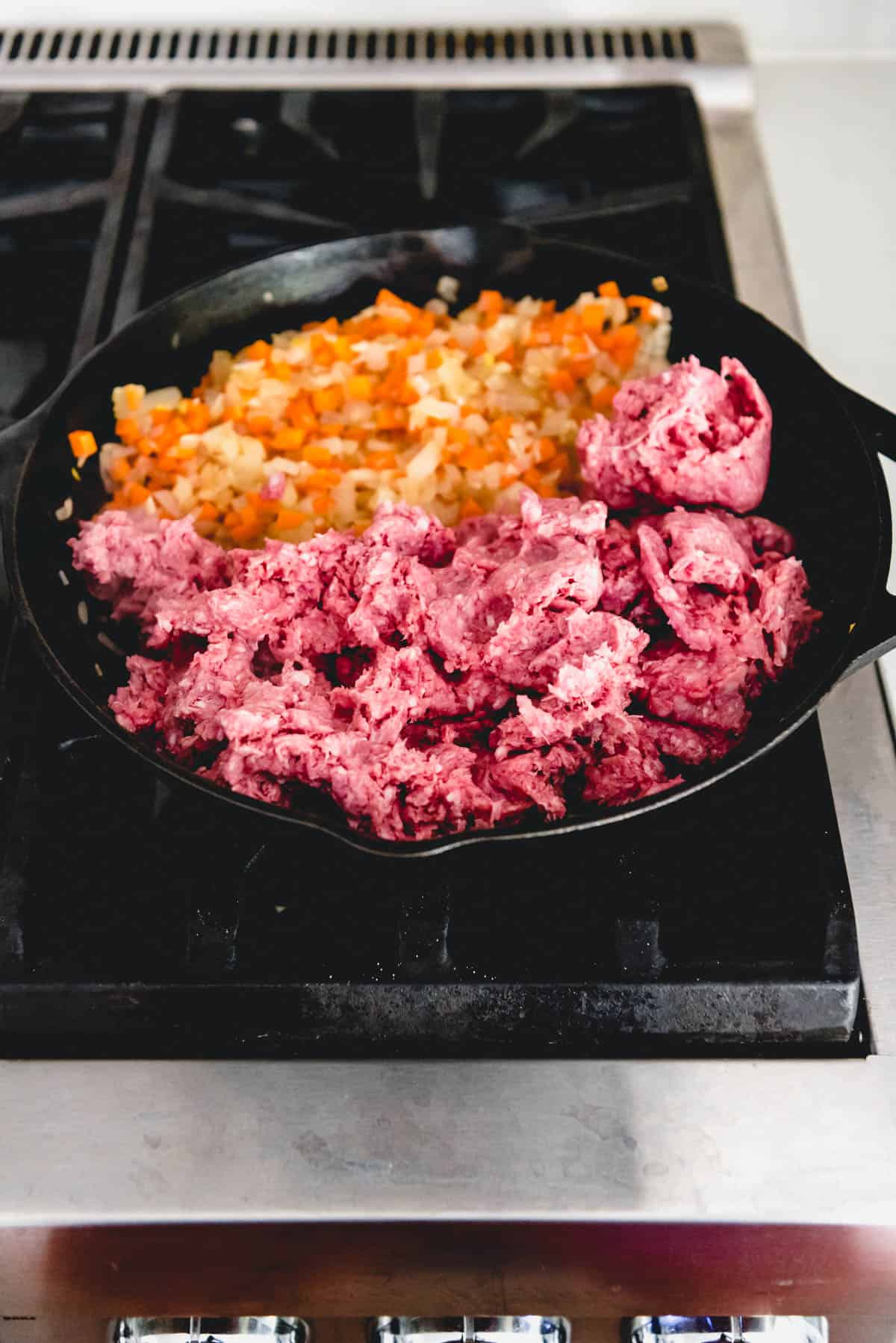 Adding ground lamb to a cast iron skillet with carrots and onions.