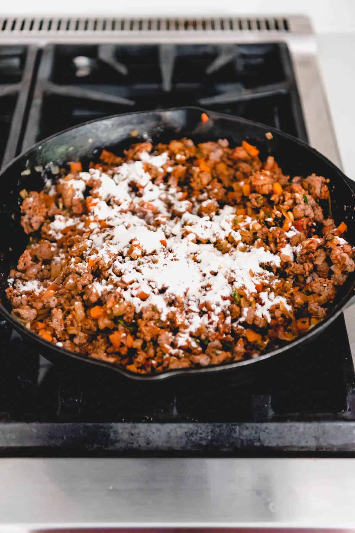 Flour sprinkled over a ground lamb mixture in a cast iron skillet.