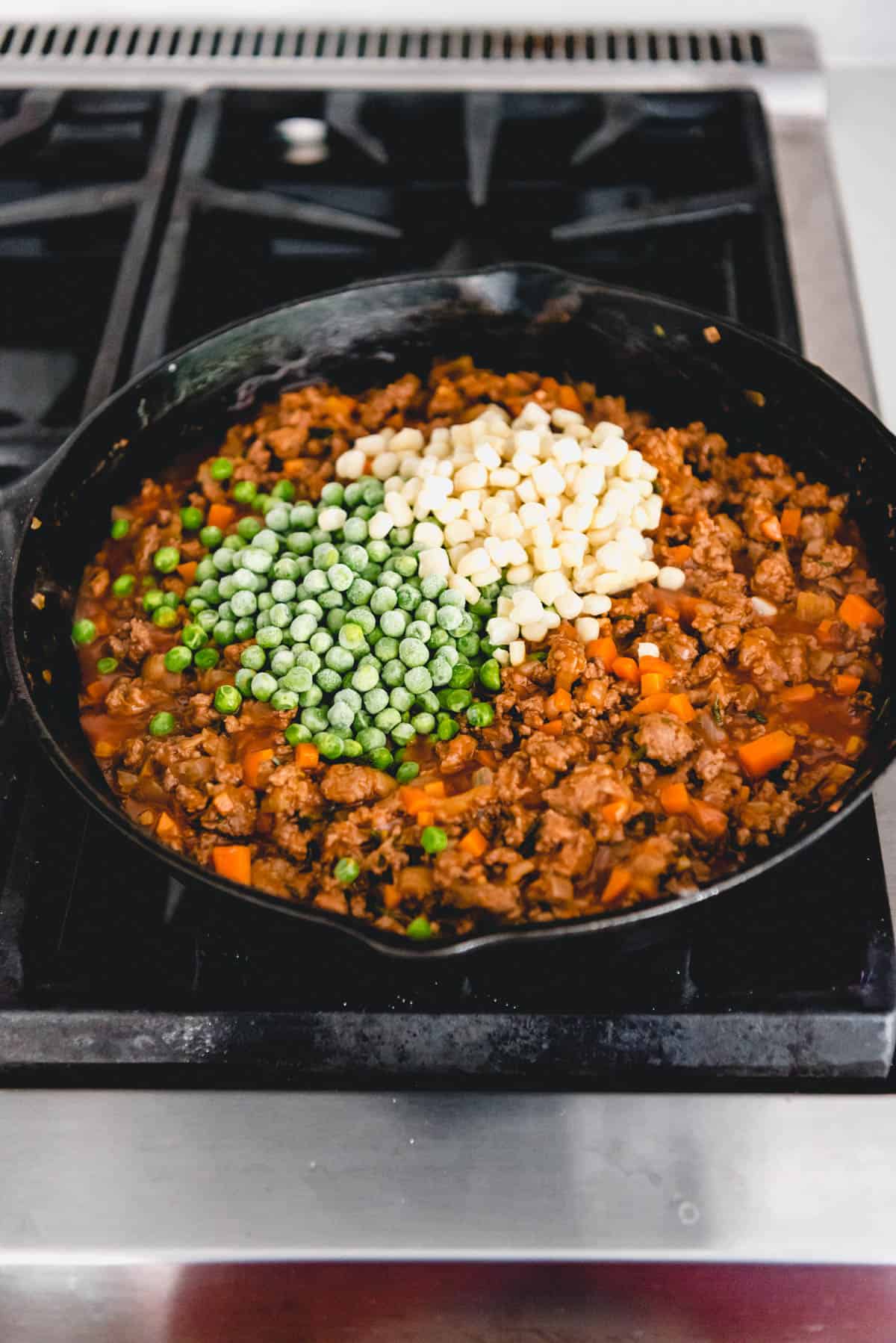 Adding frozen peas and corn to make shepherd's pie filling.