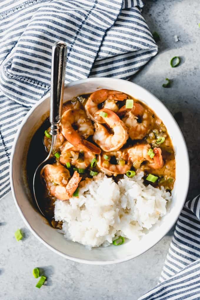 an aerial view of a white bowl filled with shrimp etouffee and white rice and a spoon