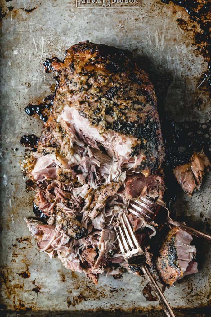 An image of pulled pork on a baking sheet being pulled apart with two forks.