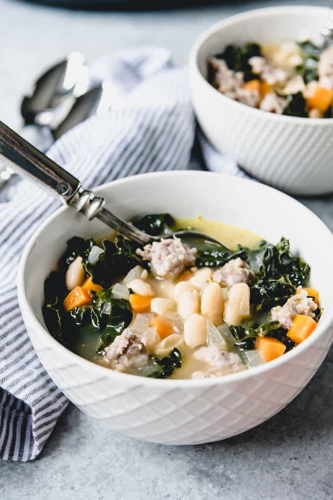 An image of a bowl of white bean soup with chopped kale, Italian sausage, and vegetables.