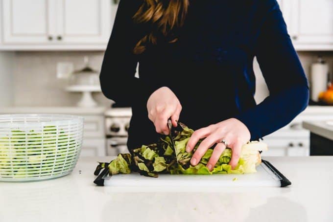 An image of hands holding a knife and a bunch of red leaf lettuce and chopping it for a mixed greens spring salad.
