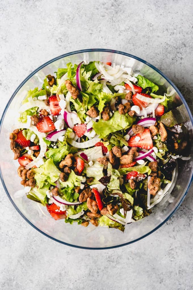 An image of a Spring salad made with sliced fresh strawberries, thinly shaved fennel, candied walnuts, chopped red onion, goat cheese, and mixed lettuce greens.
