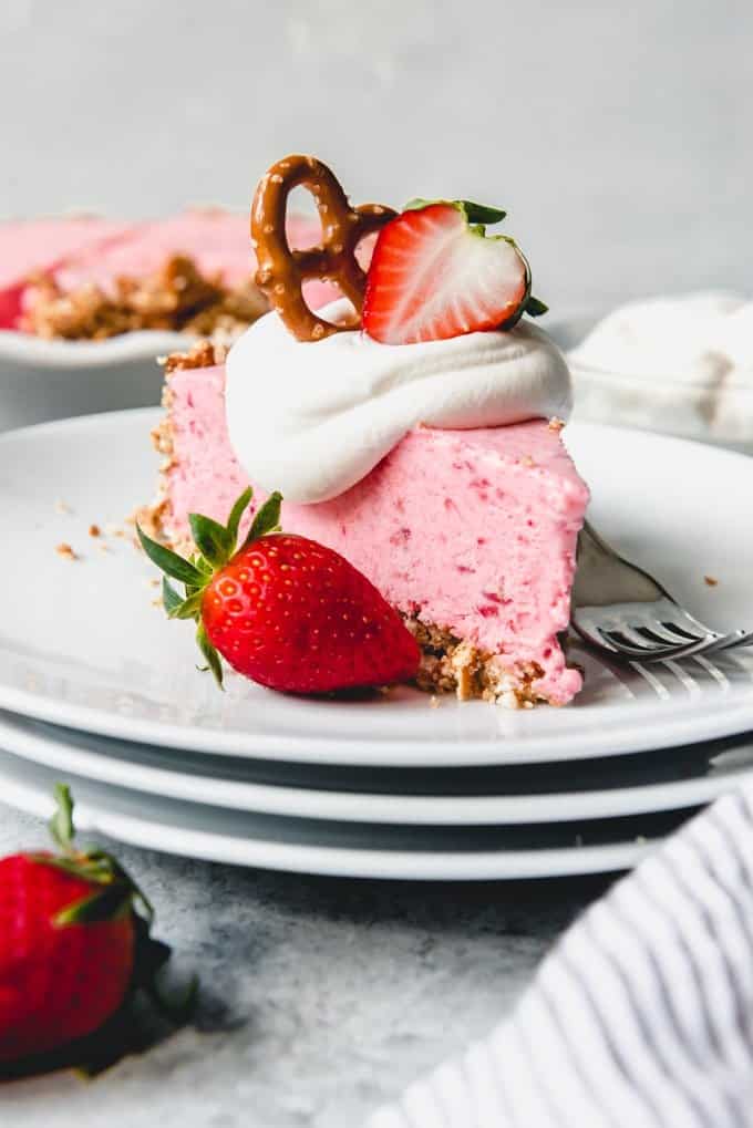 An image of light and creamy frozen strawberry pie topped with whipped cream, a pretzel, and a strawberry.
