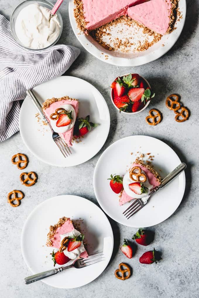 An image of three slices of frozen strawberry icebox pie topped with whipped cream, strawberries, and pretzels.