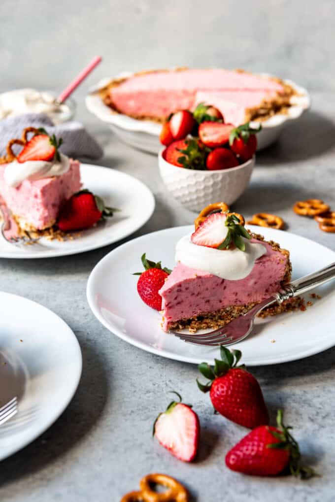 fresh strawberries and whole pretzels around and garnishing slices of Strawberry Pretzel Icebox Pie on white plates