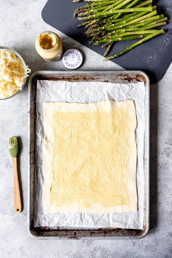 An image of puff pastry brushed with Dijon mustard on a baking sheet lined with parchment paper.