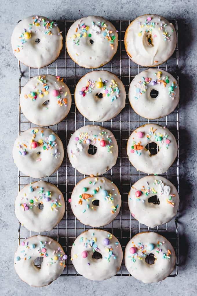 An image of homemade sprinkle donuts in rows on a wire rack. 