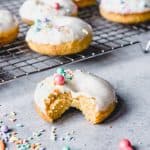frosted carrot cake donuts on a wire rack with sprinkles and one in front with a bite missing