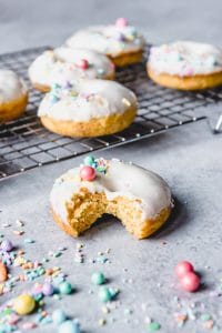 frosted carrot cake donuts on a wire rack with sprinkles and one in front with a bite missing