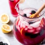 blackberry lemonade in a pitcher with fresh lemon slices and blackberries and a filled cup in back