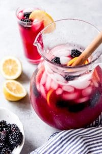 blackberry lemonade in a pitcher with fresh lemon slices and blackberries and a filled cup in back