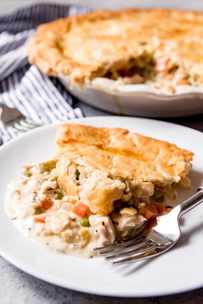 a slice of chicken pot pie on a white plate with a fork and more pie in the background