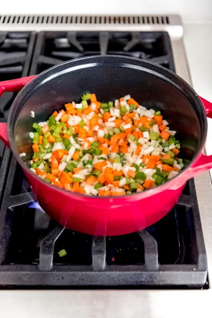An image of carrots, onions, celery, and peas being cooked in a large pan on the stove for chicken pot pie filling.