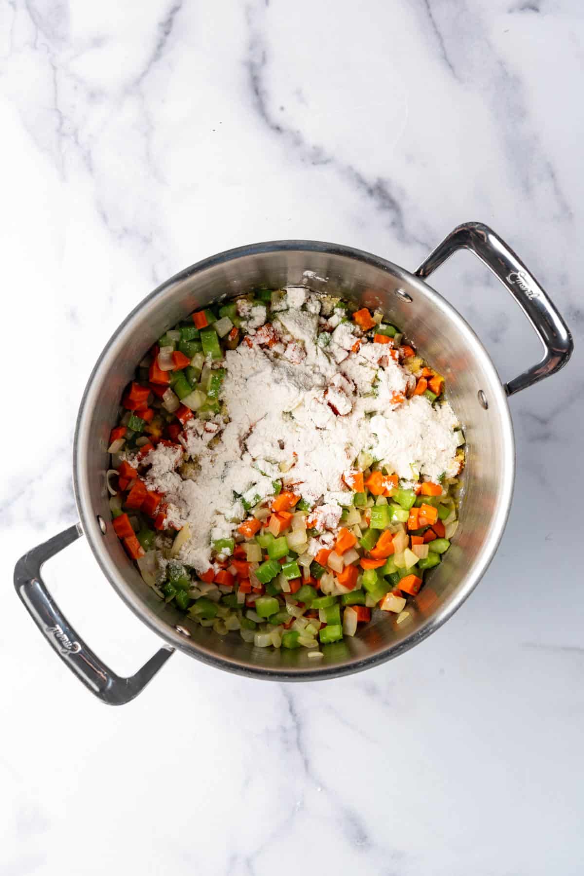 Adding flour to sauteed vegetables in a large pot.