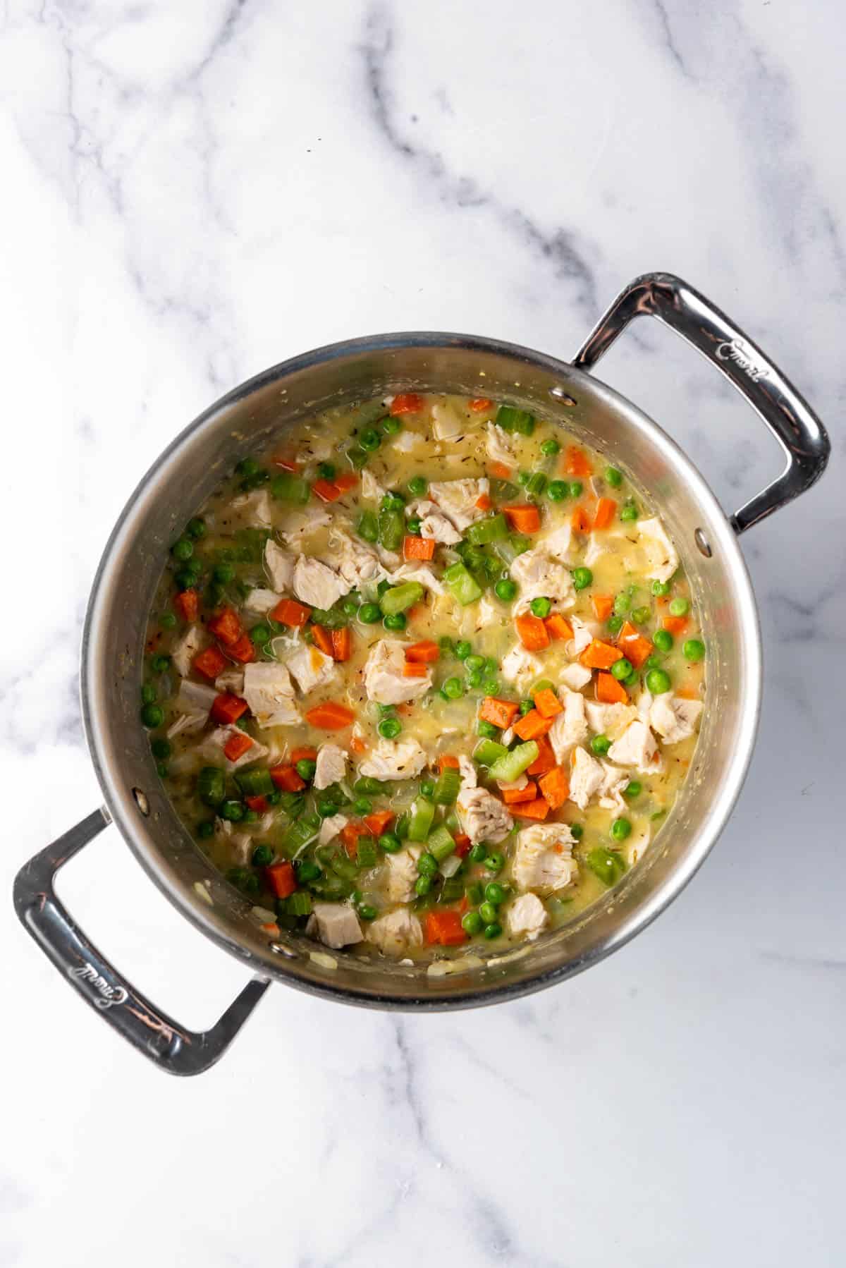 Chicken broth added to the vegetables for chicken pot pie filling in a large pot.