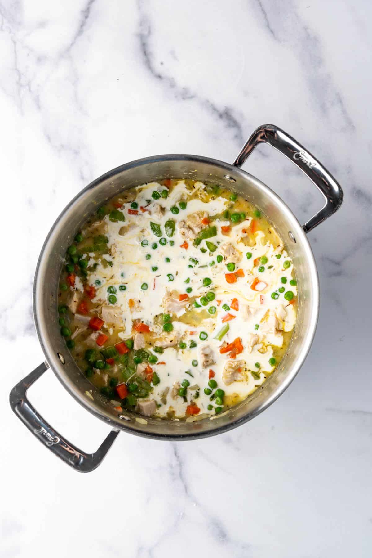 Adding heavy cream to chicken pot pie filling.