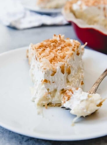 A slice of coconut cream pie on a plate with a bite taken out of it