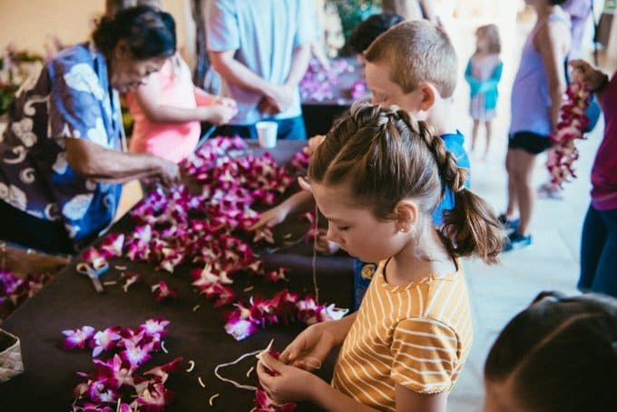 kids and adults stringing together flowers for a hawaiian necklace