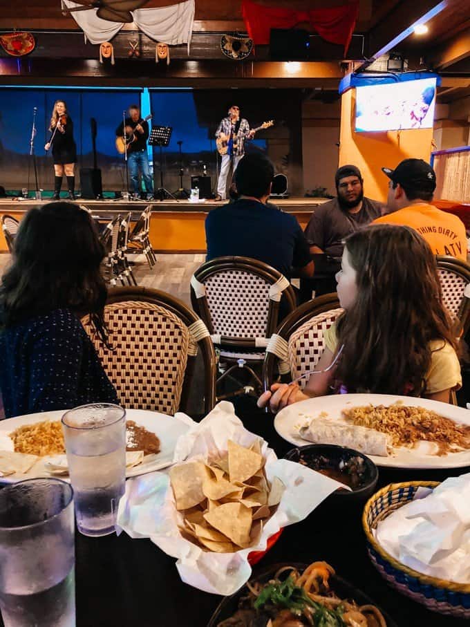 two girls at a table with food turning their heads back to watch a live band playing music