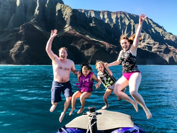 a family of 4 all jumping up above water and in front of a hilly landscape