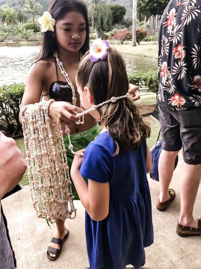 a girl getting a beaded shell necklace put on
