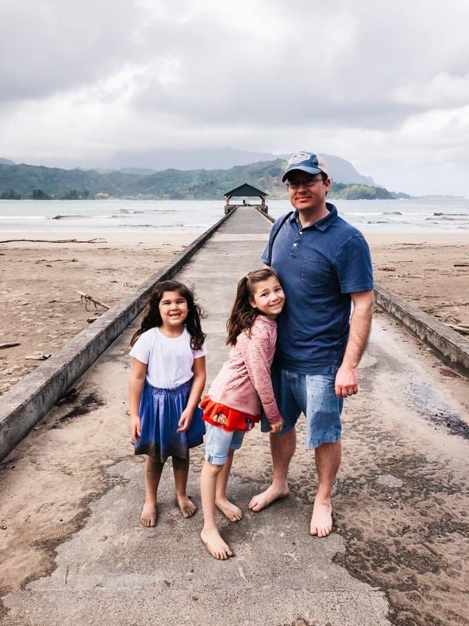 a man and his daughters standing on a walkway at the beach