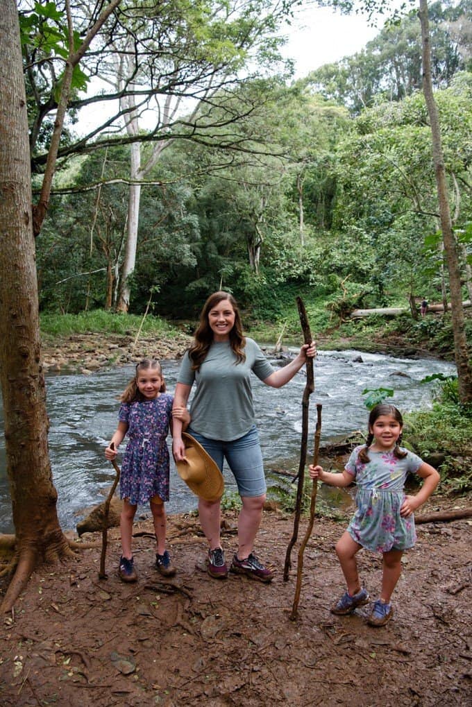 a woman and 2 girls holding walking sticks near the river