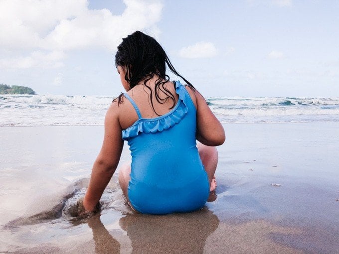 a girl in a blue bathingsuit playing in the sand at the beach