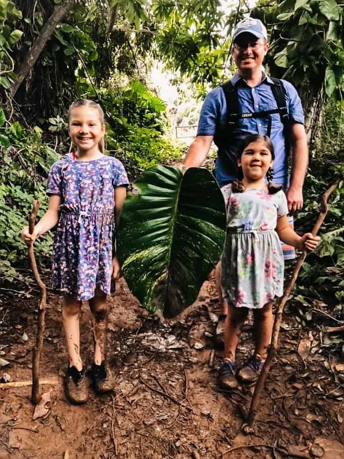a man and two girls on a walking trail holding sticks and a giant leaf