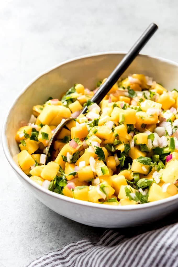 An image of a bowl of fresh mango salsa with a spoon in it.