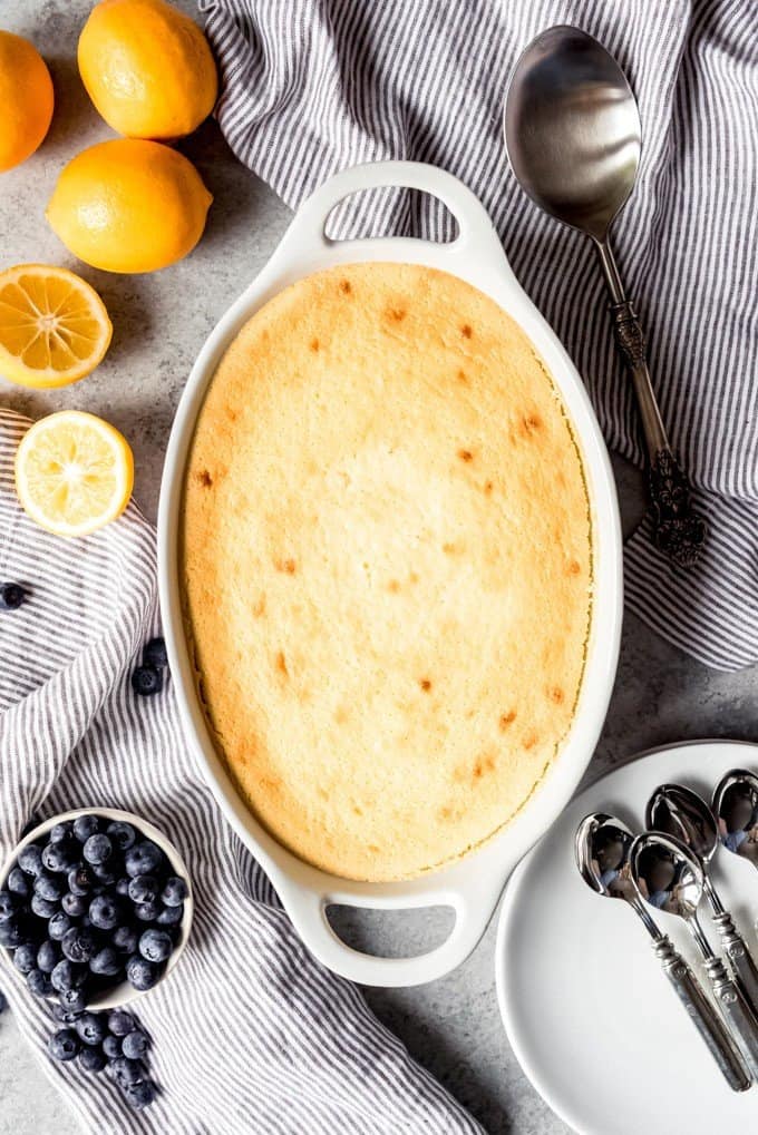 An image of a Meyer lemon pudding cake right out of the oven with Meyer lemons and blueberries next to it.