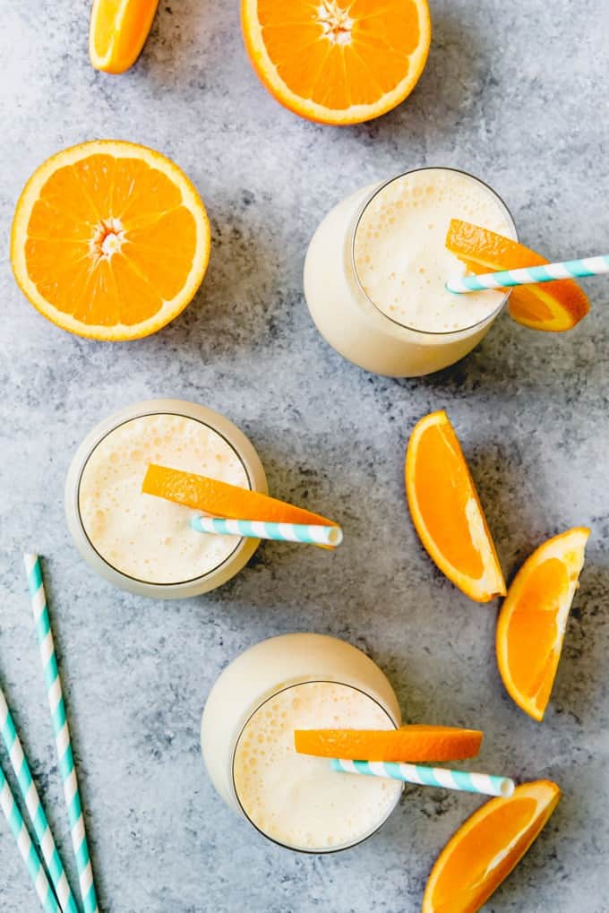 aerial view of glasses filled with orange julius with sliced oranges and striped straws