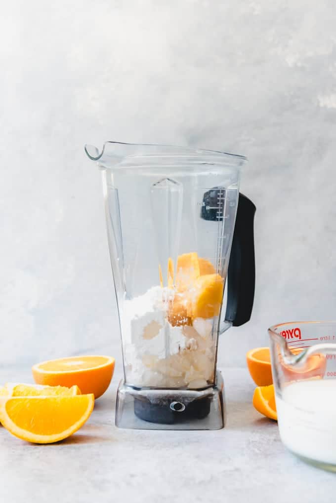 a blender filled with ingredients with a liquid measuring glass and sliced oranges to the sides