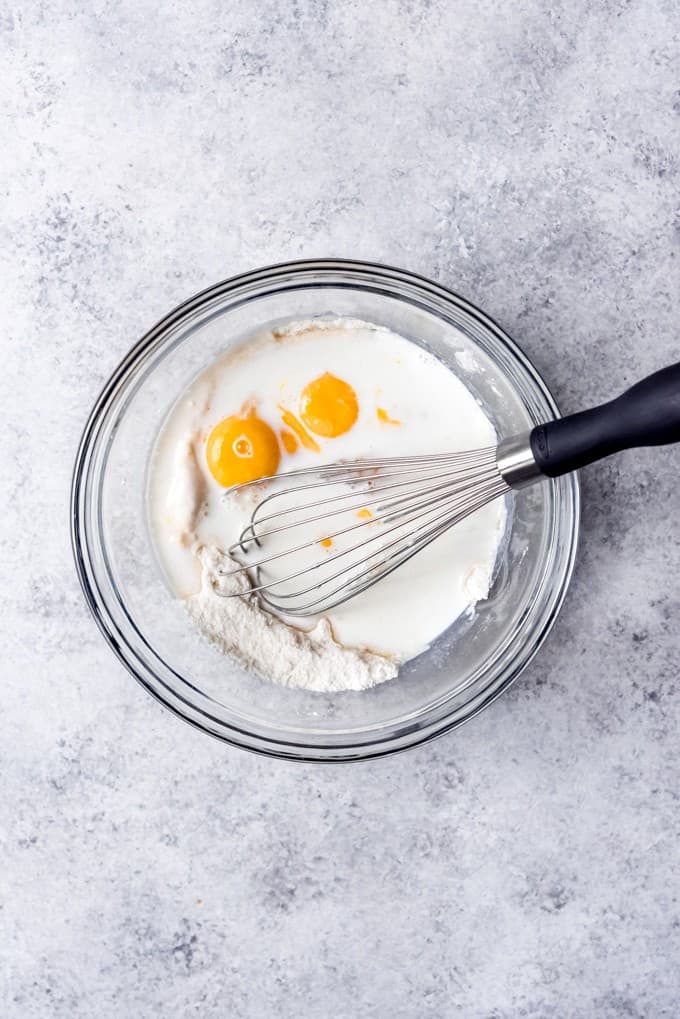 An image of flour, sugar, egg yolks, and milk in a bowl with a whisk.