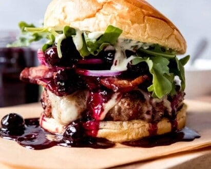 A Red, White, and Blueberry Bacon Burger with Basil Aioli on a piece of parchment paper on top of a wooden cutting board