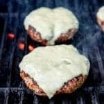 Burgers with cheese on a grill over flames.