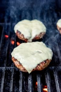 Burgers with cheese on a grill over flames.