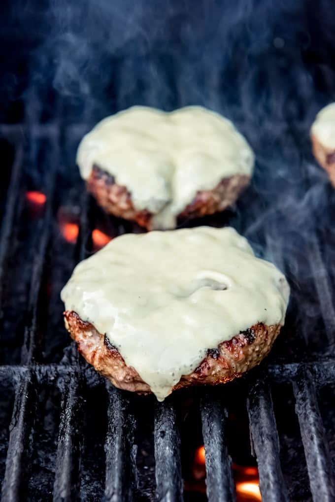 An image of grilled hamburger patties with slices of havarti cheese melting on top.