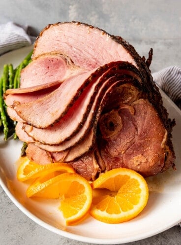 An image of a large sliced ham on a white platter with orange slices.