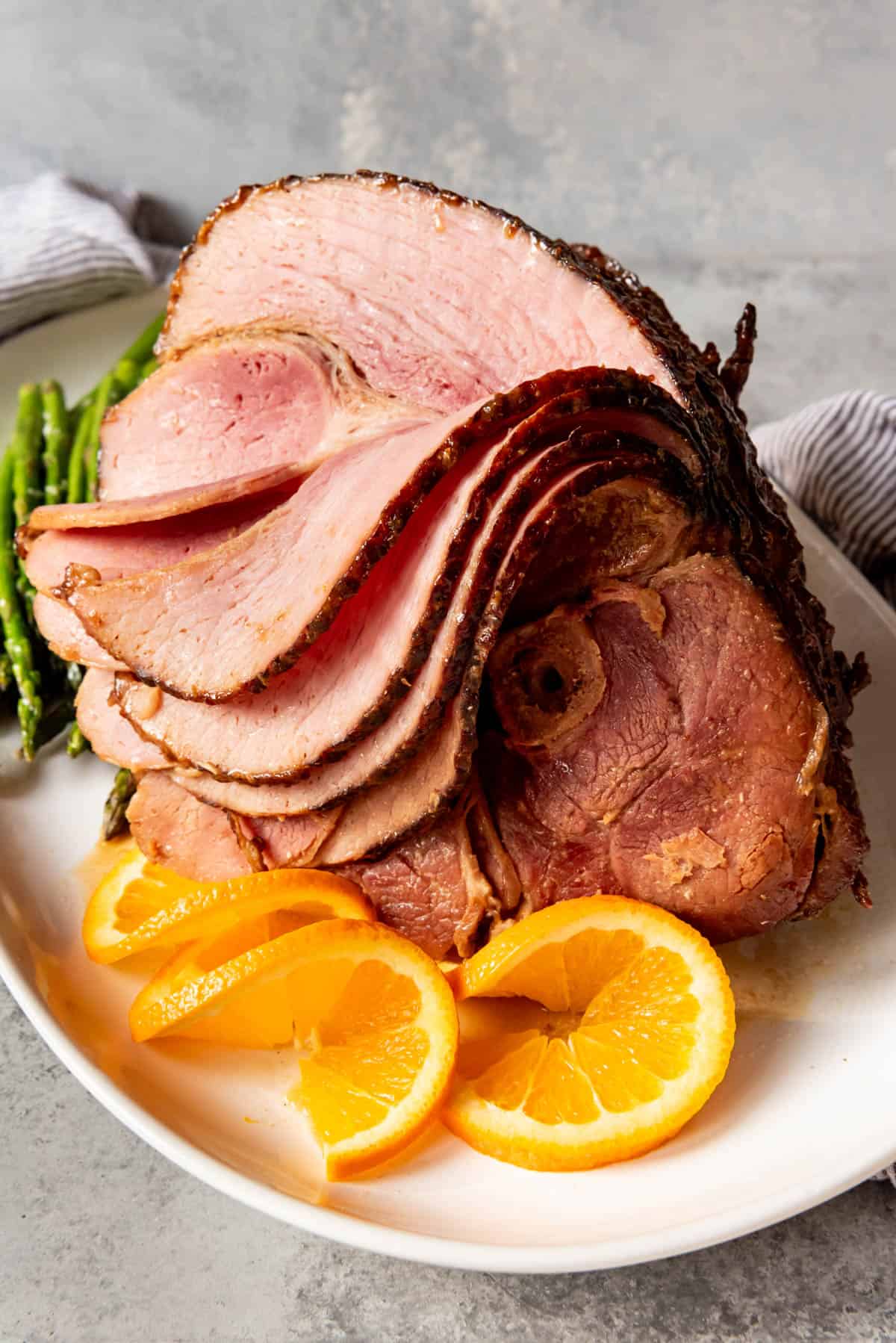 An image of a large sliced ham on a white platter with orange slices.