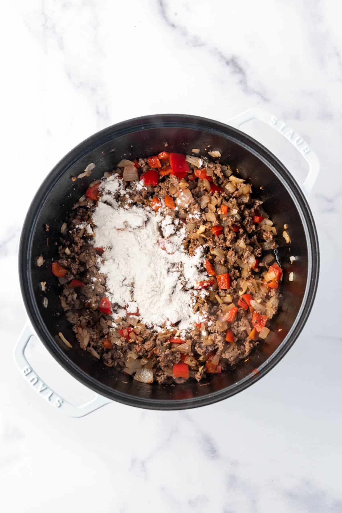 Floured sprinkled over a pot of ground beef, vegetables, and spices.