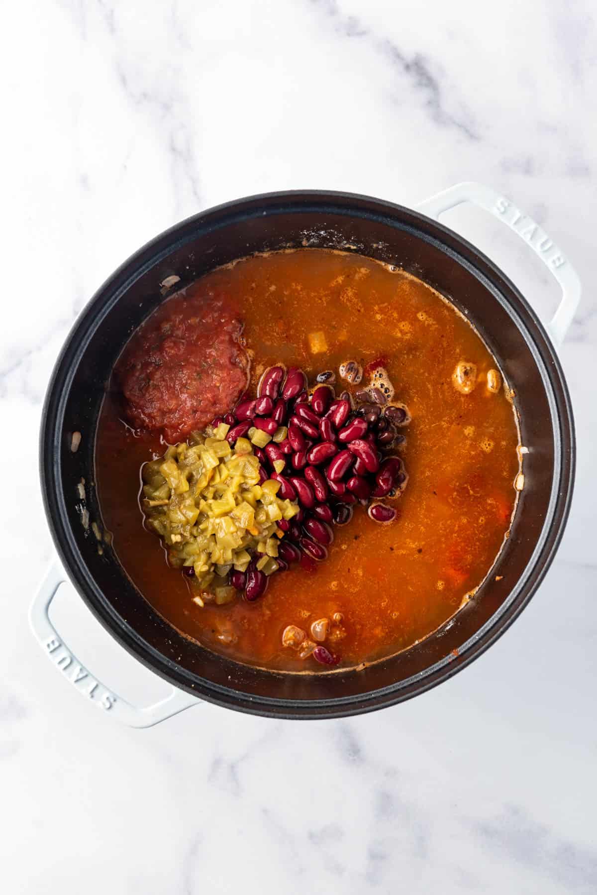 Adding liquid, beans, and diced green chilis to a pot of taco soup.