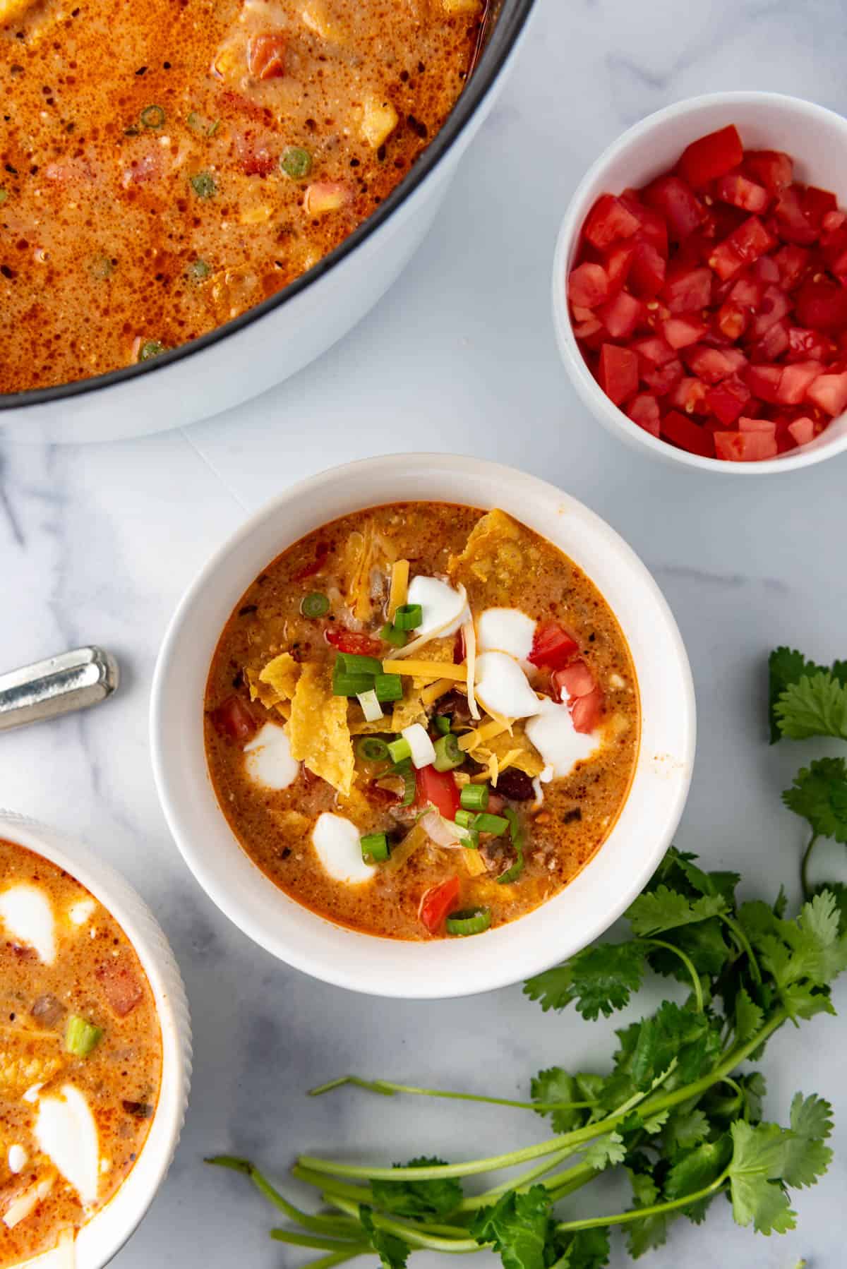 An overhead image of a bowl of cheesy taco soup next to fresh cilantro and a bowl of diced tomatoes.