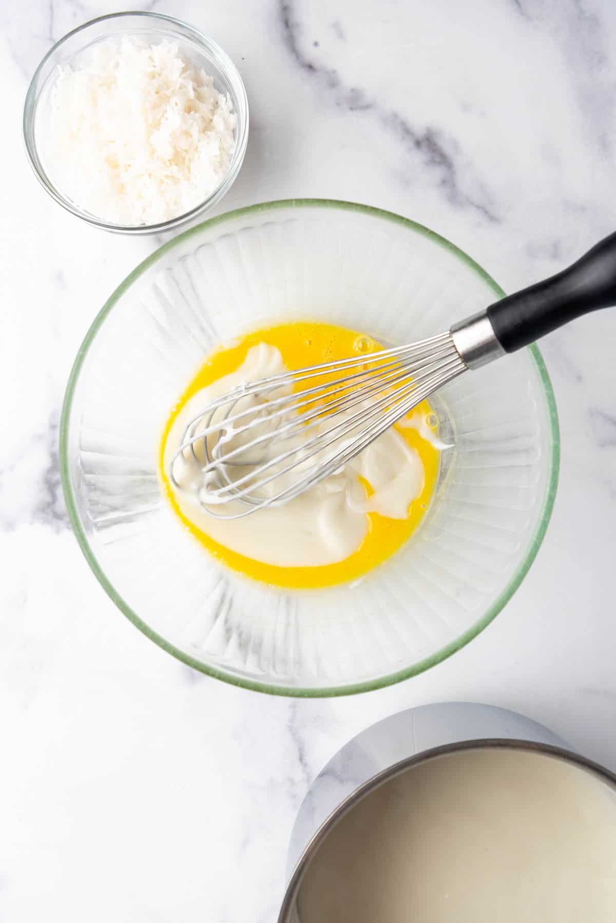 Whisking thickened hot cream mixture into egg yolks in a glass mixing bowl.