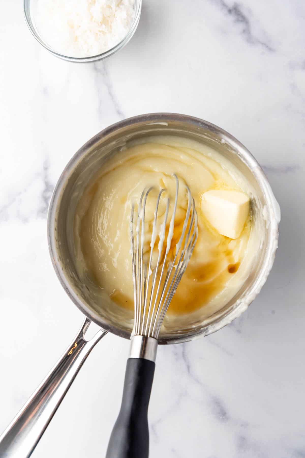 Whisking vanilla and butter into custard in a saucepan.