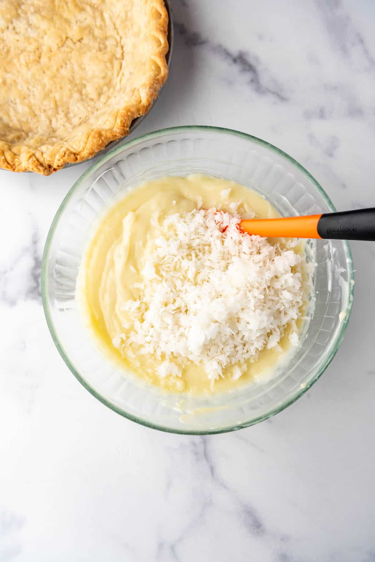 Adding shredded sweetened coconut to custard in a glass mixing bowl.