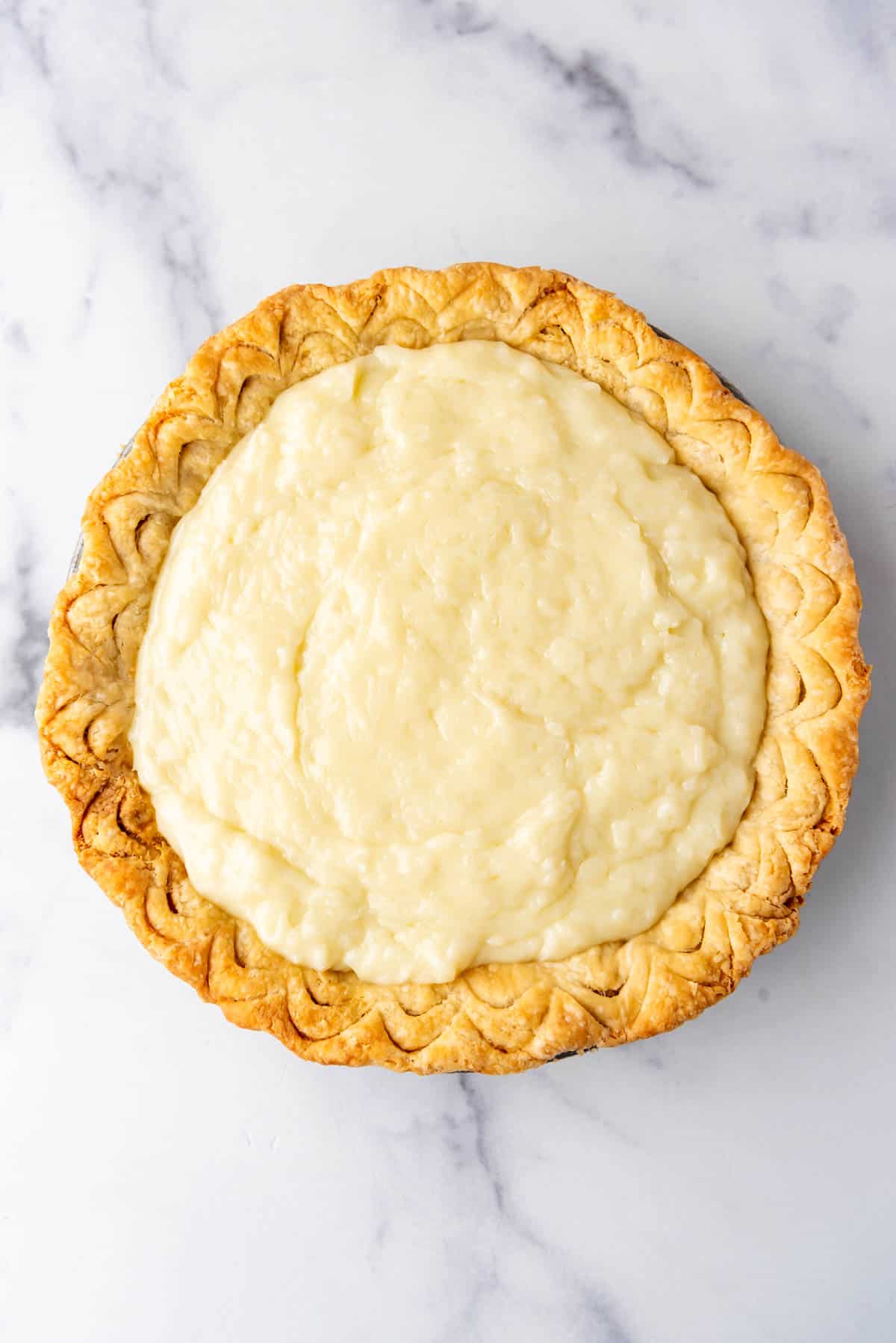 Pouring coconut cream filling into a baked pie crust.